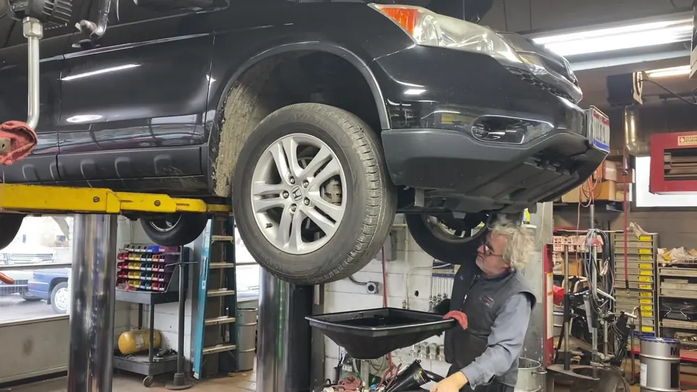 A mechanic working beneath an SUV raised on a lift in the shop