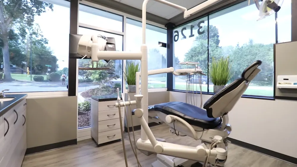 Dental treatment room with a navy patient chair beside a large window